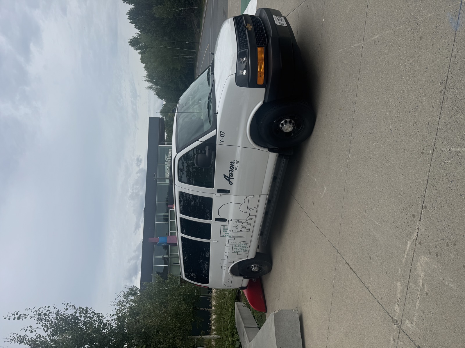 White Aaron Shuttle van with its city line-art wrap, parked on campus